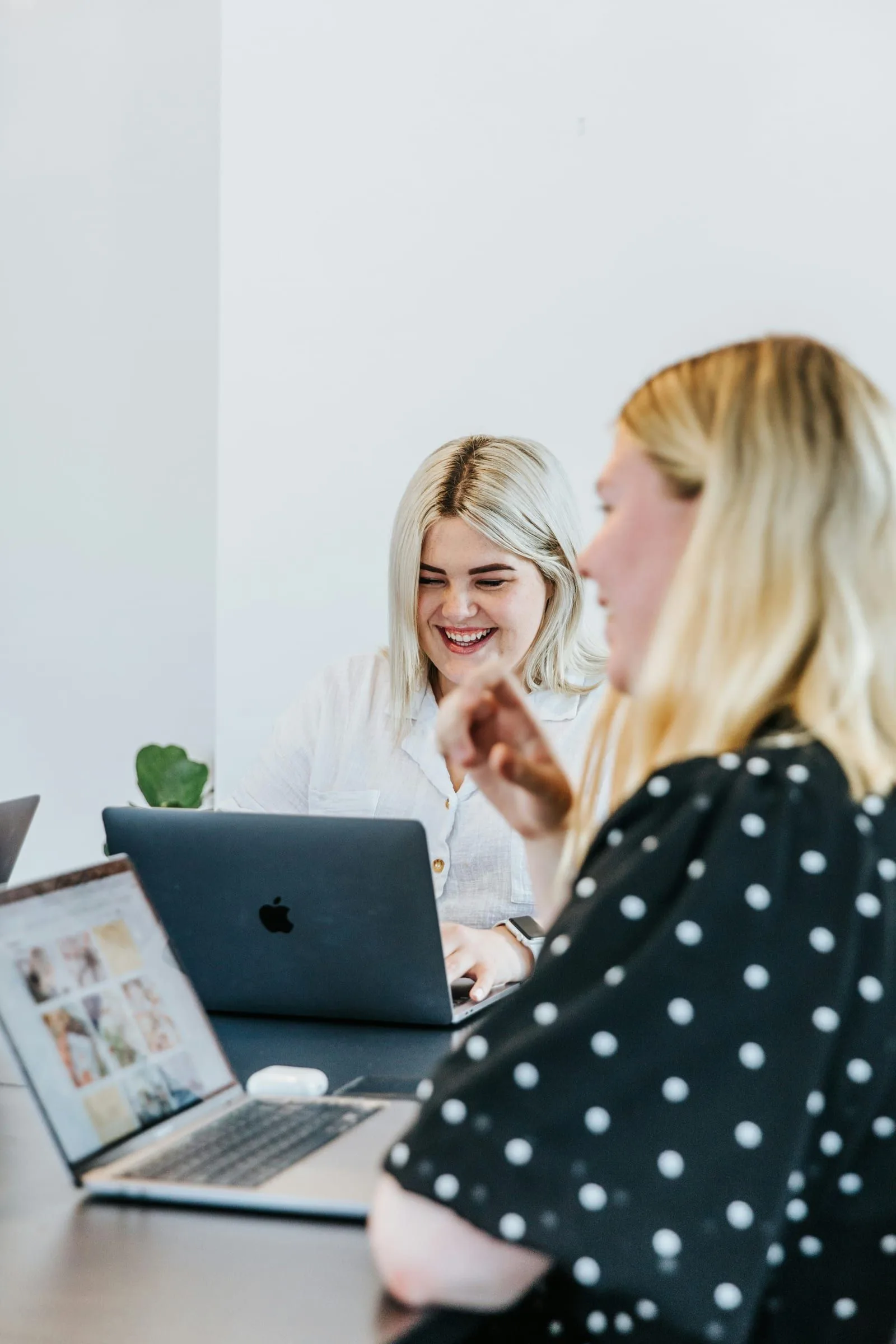 Zwei Kolleginnen arbeiten lachend gemeinsam an Laptops an einem Tisch